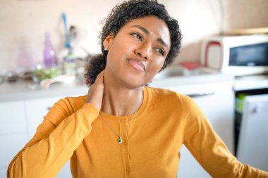 Yorgun siyah kadın evde çalışıyor ve boynu ağrıyor.