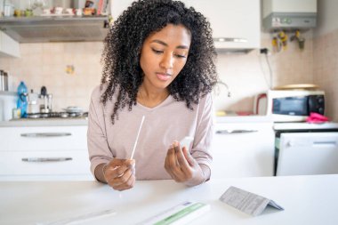 Siyahi bir kadın evde kendi kendine covid-19 testi yapıyor.