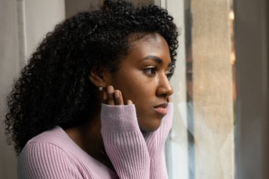 Siyahi bir kadın çok üzgün dua ediyor pencerenin önünde düşünerek