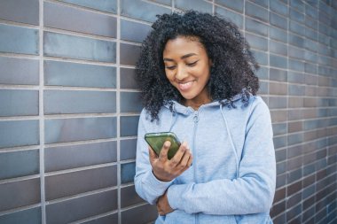 Caddede elinde cep telefonu tutan gülümseyen siyah bir kız.