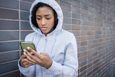 Üzgün, genç, siyah bir kız cep telefonuyla mesajlaşıyor.