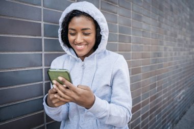 Şehir caddesinde cep telefonuyla mesajlaşan mutlu siyah kız.