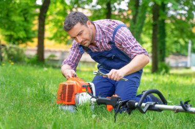 Bahçedeki kırık çalı kesiciyi tamir eden bir adam.