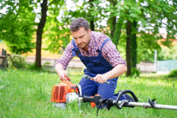 Bahçedeki kırık fırça kesiciyi tamir eden bir adam.