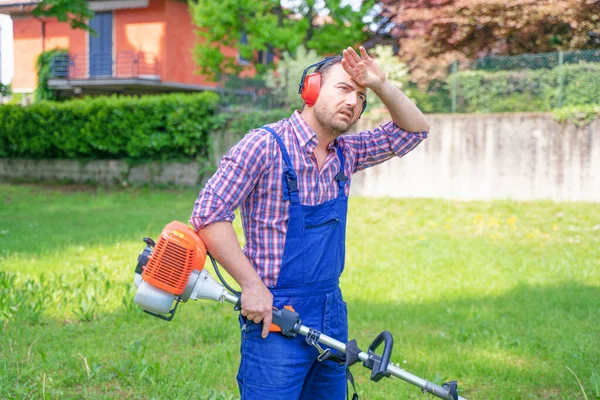 Bahçede çalışan ve çim biçme makinesi kullanan bir adam.