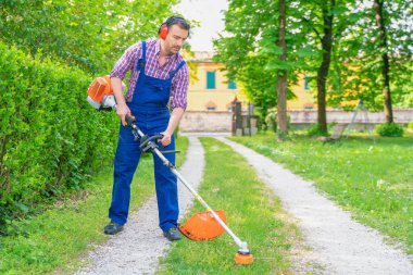 Bahçede çalışan ve çim biçme makinesi kullanan bir adam.