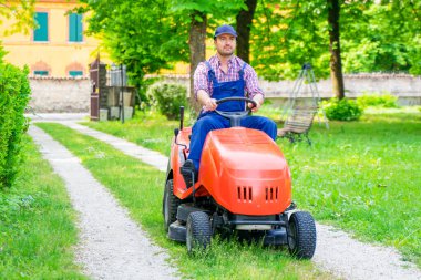 Bir bahçıvan çim biçme makinesi bahçesine biniyor.