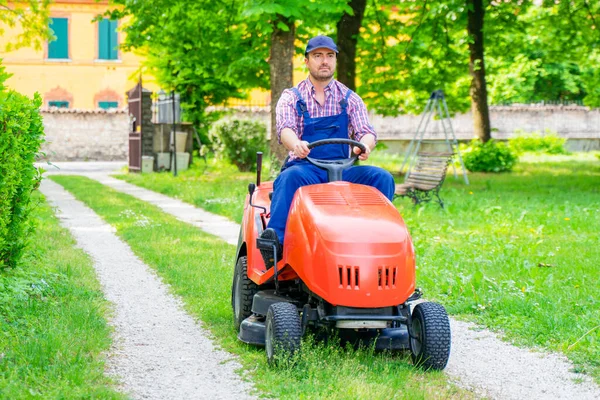 Bir bahçıvan çim biçme makinesi bahçesine biniyor.
