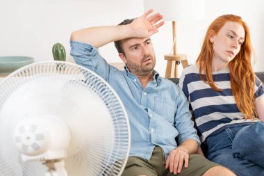 Overheated couple sitting on couch and feeling unwell suffering from heating at home