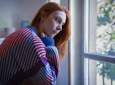Depressed woman sitting on sofa at home, feeling blue