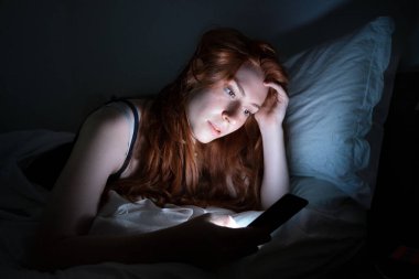 Bir kadın cep telefonunu gece geç saatlerde yatakta tutuyor.