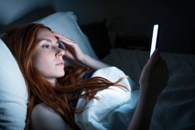 Gece geç saatlerde yatakta akıllı telefon kullanan bir kadın.
