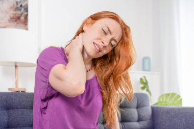 Başı ve boynu ağrıyan bir kadın evdeki kanepede oturuyor.