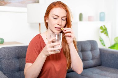 Kadın evdeki kanepede otururken vitamin alıyor.
