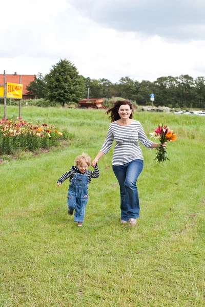 Jovem mãe e seu filho correndo através do campo com buquê de lírio — Fotografia de Stock