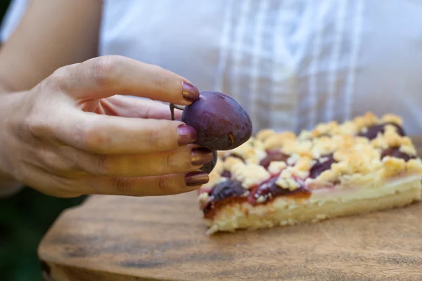 Ameixa fresca na mão da mulher com torta de ameixa no fundo — Fotografia de Stock