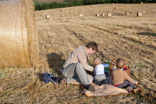 Mladý otec a dva chlapce dělat piknik na slaměné pole — Stock fotografie