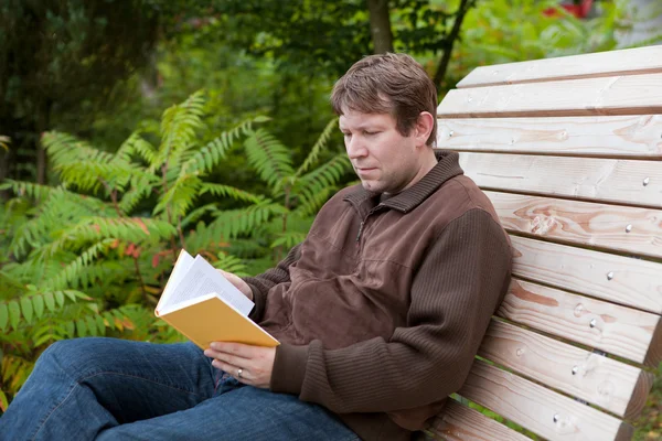 Young man reading book on bench in autumn forest — Stock Photo, Image