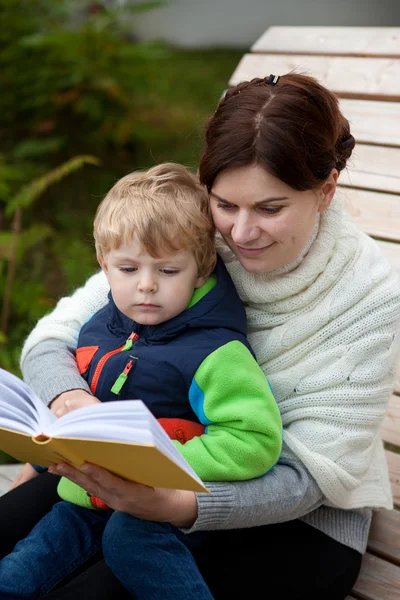 Jonge moeder en peuter zoon lezen boek op Bank buiten — Stockfoto