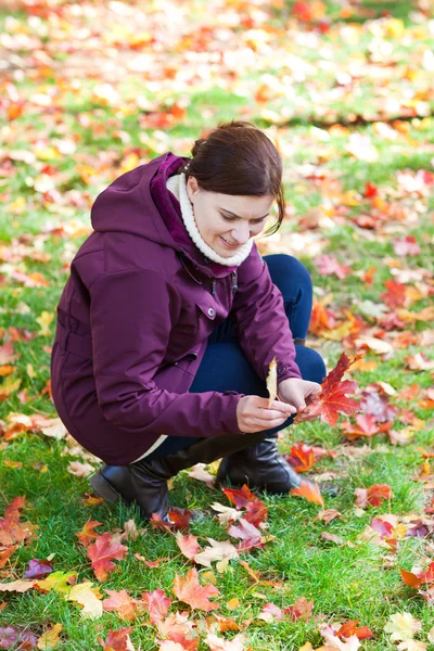 Bella donna nel parco autunnale raccoglie foglie — Foto Stock