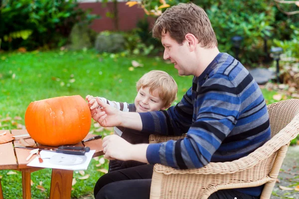 Hombre joven y niño pequeño haciendo calabaza de halloween — Foto de Stock