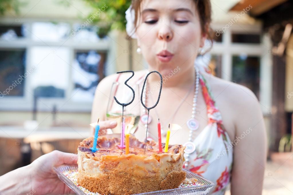 Young woman blowing out birthday candles 30