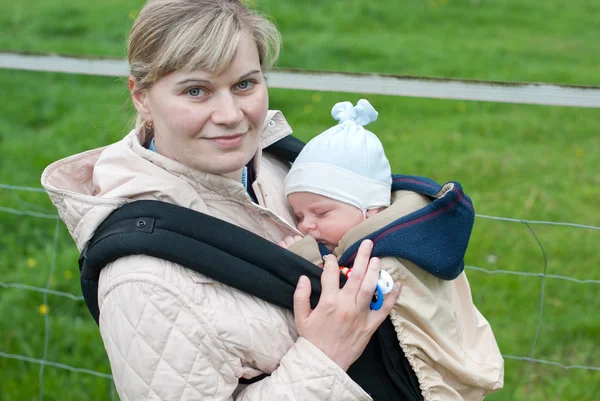 Молода мати носить маленьку дитину в рюкзаку в парку — стокове фото