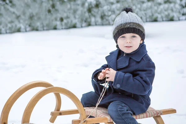 Прекрасный маленький мальчик на древних санях в зимний день — стоковое фото