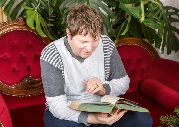 Young man reading book on red couch indoor — Stock Photo, Image