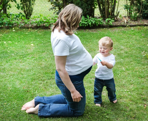 Молода вагітна жінка і маленький син в літньому саду — стокове фото