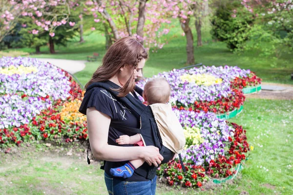 Young mother carrying baby son in rucksack in park — Stock Photo, Image