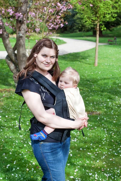 Young mother carrying baby son in rucksack in park — Stock Photo, Image