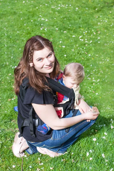 Young woman carrying baby in rucksack in park — Stock Photo, Image