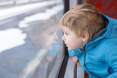 Cute little boy looking out train window clipart