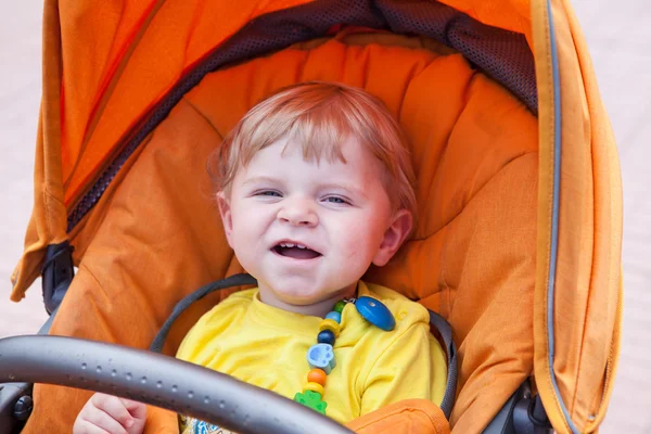 Beau tout-petit garçon souriant en plein air en poussette orange — Photo