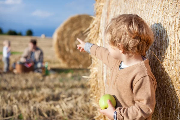 Pequeño niño comiendo manzana con una gran paca de heno en el campo —  Fotos de Stock