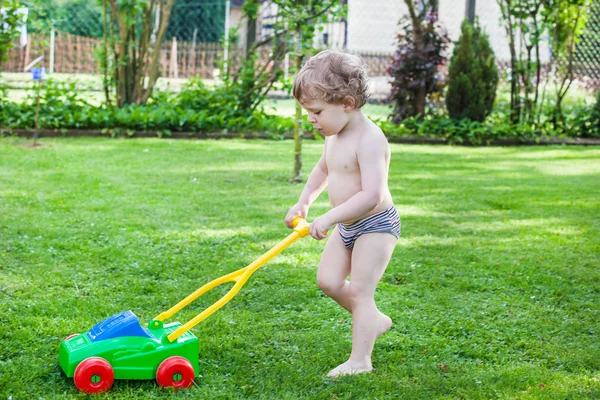 Little blond toddler boy playing with lawn mower