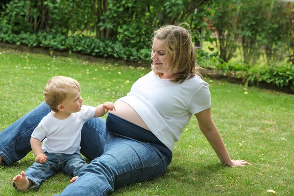 Mujer embarazada y pequeño hijo en el jardín de verano —  Fotos de Stock