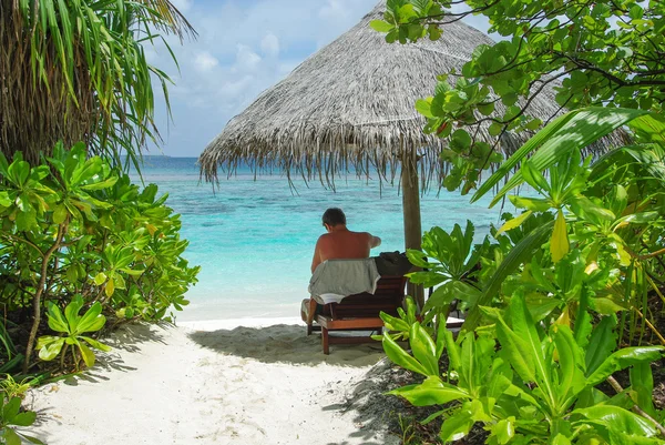 Muž sedící pod deštníkem na krásné pláži — Stock fotografie