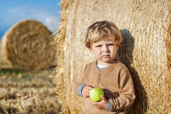 Little toddler eating apple with a big hay bale on field — Stock Photo, Image