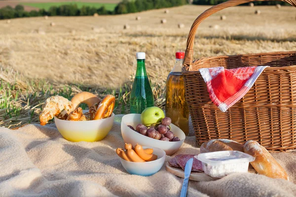 Cesta de piquenique e diferentes alimentos e bebidas no campo de palha — Fotografia de Stock