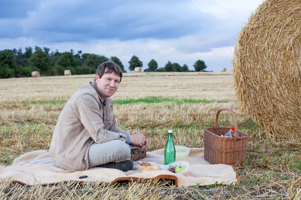 Mladý muž dělat piknik na seno pole — Stock fotografie