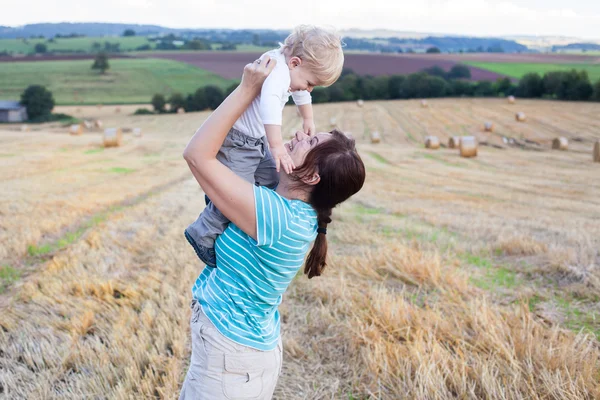 Young mother and her little son having fun in straw field — Stock Photo, Image