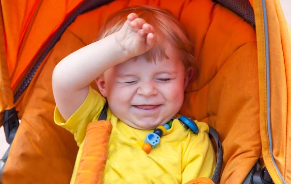 Прекрасний маленький хлопчик посміхається на відкритому повітрі в помаранчевій колясці — стокове фото