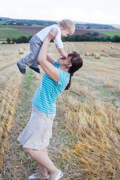 Young mother and her little son having fun in straw field — Stock Photo, Image