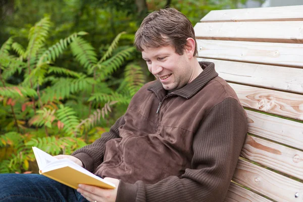 Young man reading book on bench in summer forest — Stock Photo, Image