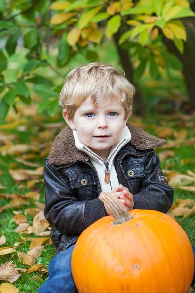 Kleine peuter met grote oranje pompoen in tuin — Stockfoto