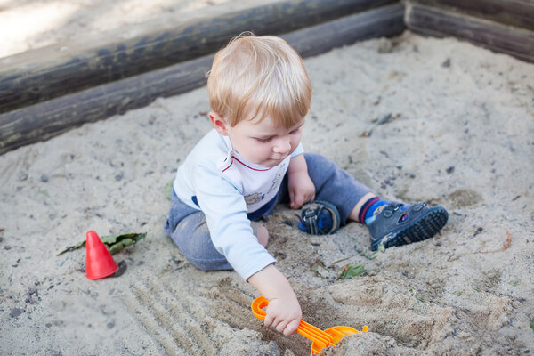 Little toddler boy playing with sand and toy