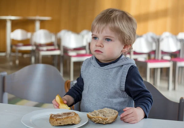 Маленький мальчик ест хлеб и яблоко в детской школе — стоковое фото