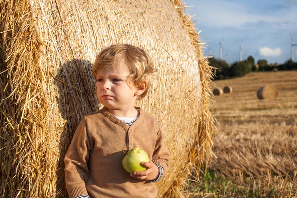 Kleine peuter eten apple met een grote hooi baal op veld — Stockfoto